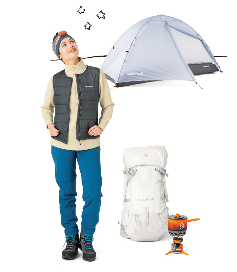 アイボリーのプルオーバーの上にグレーのベストを着用し、青い長ズボンを履いた女性モデル。頭にオレンジのヘッドランプを付けている。背後には山岳用テントがたっていて、女性モデルの横には白い大型バックパックとバーナーがある